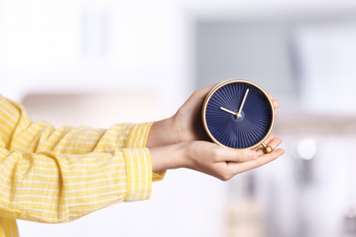 Young woman holding alarm clock on blurred background. Time concept