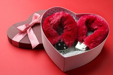 Gift box with furry handcuffs on red background