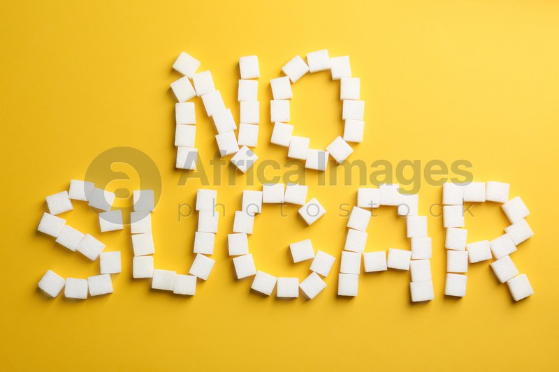 Phrase No Sugar made of refined cubes on yellow background, flat lay