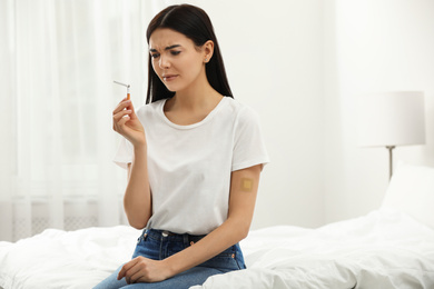 Emotional young woman with nicotine patch and cigarette in bedroom