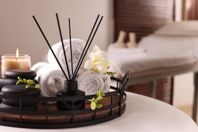 Aromatic reed air freshener, rolled towels, spa stones and candle on white table indoors