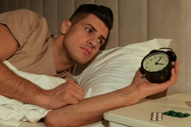 Man suffering from insomnia looking at time on alarm clock in bed indoors
