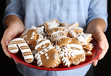 Photo of Woman with plate of delicious gingerbread Christmas cookies on black background, closeup
