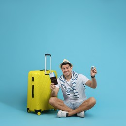 Male tourist holding passport with ticket and toy airplane near suitcase on turquoise background, space for text