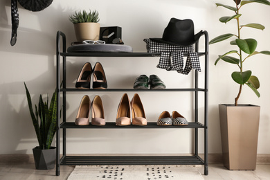 Black shelving unit with shoes and different accessories near white wall in hall