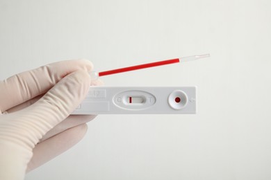 Doctor holding disposable express test for hepatitis and pipette with blood on white background, closeup