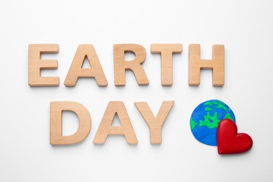 Phrase Earth Day of wooden letters and red heart with planet model on white background, top view