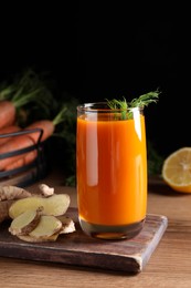 Photo of Glass of tasty carrot juice and ingredients on wooden table against black background