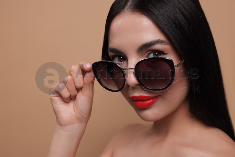 Attractive woman wearing fashionable sunglasses against beige background, closeup