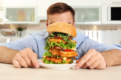 Photo of Hungry man and huge burger in kitchen