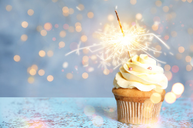 Delicious birthday cupcake with sparkler on blue table against blurred lights. Space for text