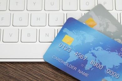 Photo of Online payment concept. Bank cards and computer keyboard on wooden table, closeup