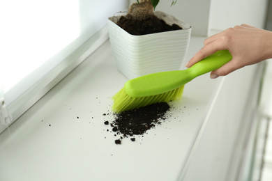 Woman sweeping away scattered soil from window sill with brush, closeup