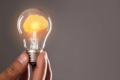 Man holding light bulb with shining brain inside against grey background, space for text. Idea generation
