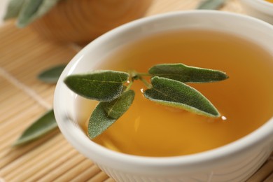 Cup of aromatic sage tea with fresh leaves on table, closeup