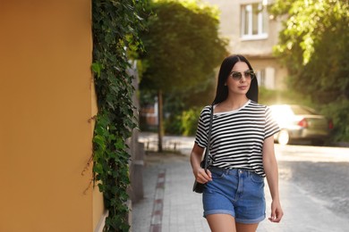 Photo of Beautiful young woman in stylish sunglasses walking on city street