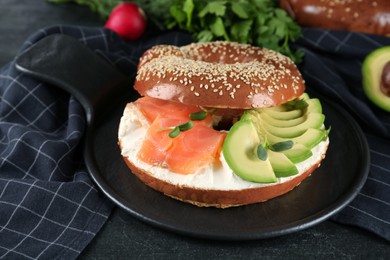 Delicious bagel with cream cheese, salmon, avocado and microgreens on black table