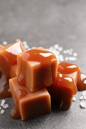 Yummy caramel candies with sauce and sea salt on grey table, closeup