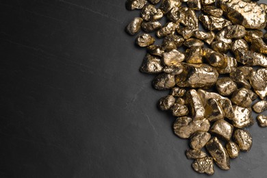 Pile of gold nuggets on black table, flat lay. Space for text