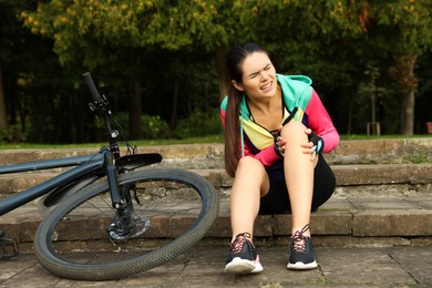 Young woman with injured knee on steps near bicycle outdoors