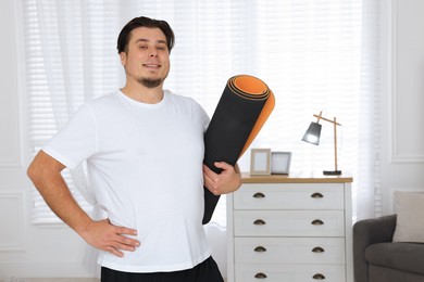 Overweight man with yoga mat at home, space for text
