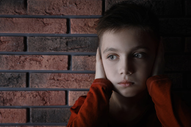 Sad little boy closing his ears near brick wall. Domestic violence concept