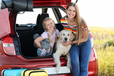 Photo of Happy mother and daughter with their dog in car trunk outdoors