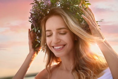 Young woman wearing wreath made of beautiful flowers outdoors