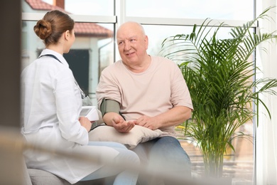 Nurse measuring blood pressure of elderly man in living room. Assisting senior generation