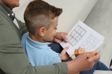 Little boy with his grandfather solving sudoku puzzle on sofa at home, closeup