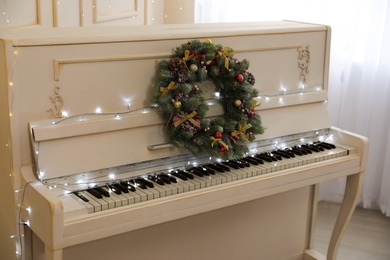 White piano with fairy lights and decorative wreath indoors. Christmas music
