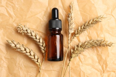 Bottle with organic cosmetic product and ears of wheat on parchment paper, flat lay