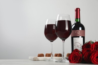 Photo of Bottle with glasses of red wine, beautiful roses and chocolate candies on white table. Space for text