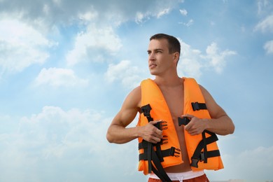 Handsome lifeguard putting on life vest against sky