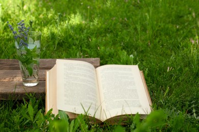 Open book with flowers in glass on green grass outdoors