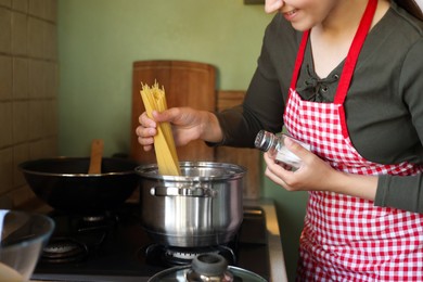 Woman cooking spaghetti on stove in kitchen, closeup