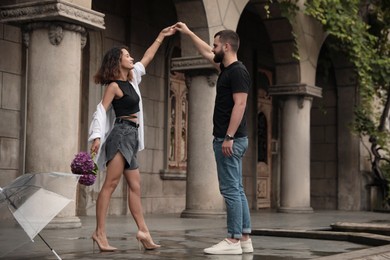 Photo of Young couple dancing under rain on city street