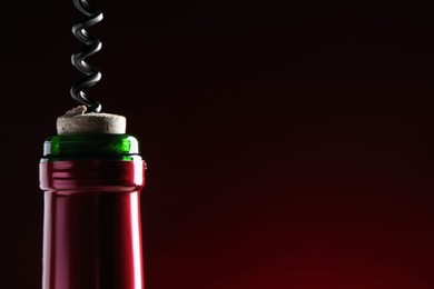 Photo of Opening wine bottle with corkscrew on dark red background, closeup. Space for text