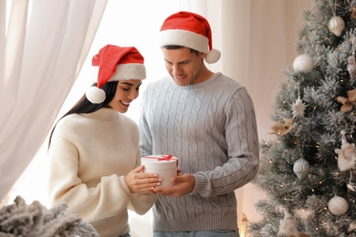 Couple in Santa hats holding gift box near Christmas tree