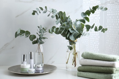Fresh eucalyptus branches and cosmetic products on countertop in bathroom