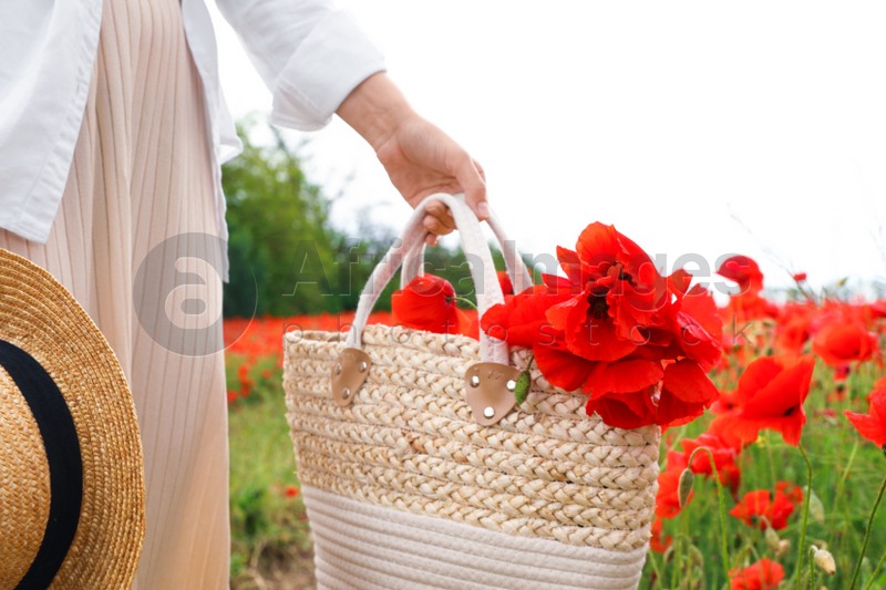 Photo of Woman holding handbag with poppy flowers in beautiful field, closeup