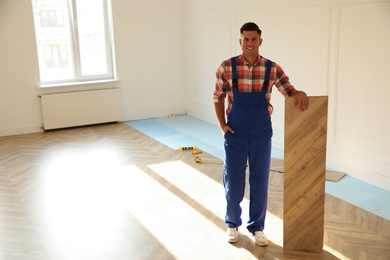 Professional worker with wooden board indoors. Installing of parquet flooring