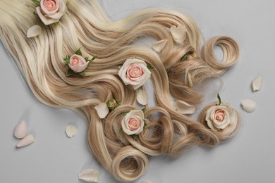 Photo of Lock of healthy blond hair with flowers on light grey background, flat lay