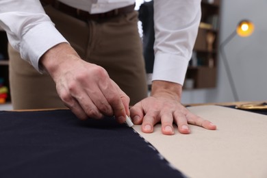Photo of Tailor marking sewing pattern on fabric with chalk at table, closeup
