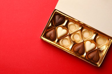 Photo of Partially empty box of chocolate candies on red background, top view. Space for text