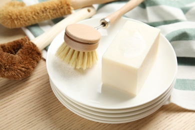 Cleaning brush, soap bar and plates on wooden table, closeup. Dish washing supplies
