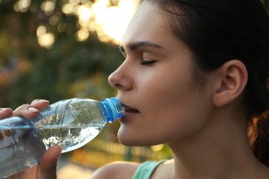 Photo of Young woman drinking water outdoors, closeup. Refreshing drink