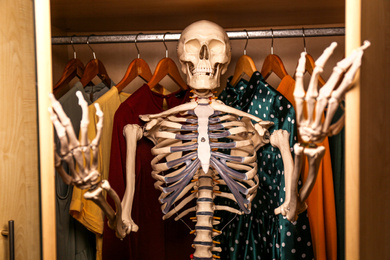 Photo of Artificial human skeleton model among clothes in wardrobe