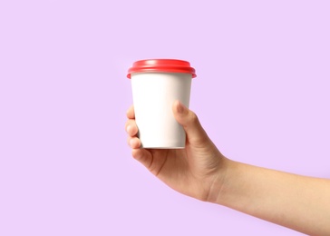 Woman holding takeaway paper coffee cup on violet background, closeup