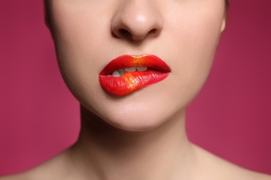 Young woman with beautiful makeup biting lip on pink background, closeup